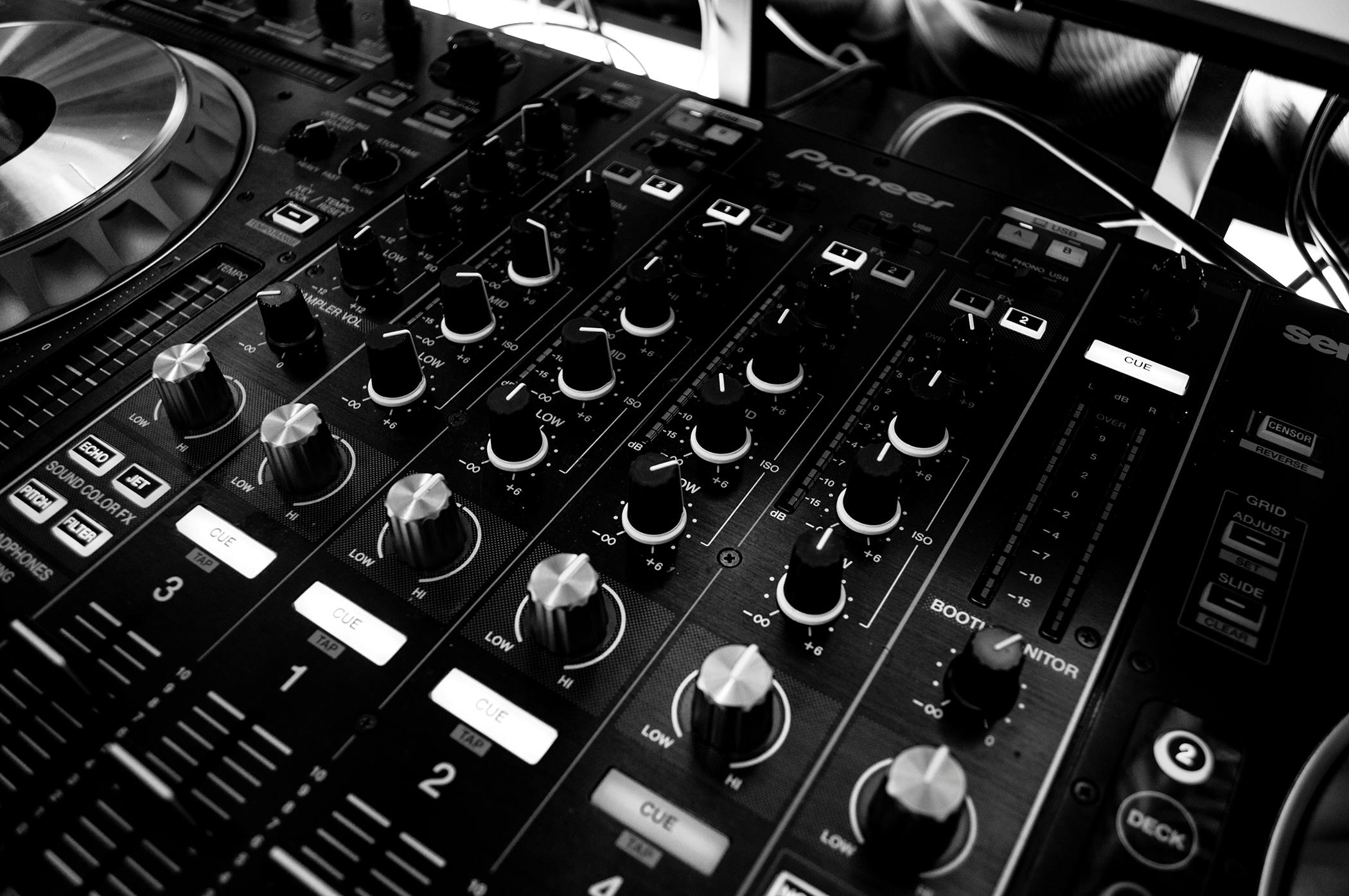 Black and white close-up of a DJ's audio mixing console with knobs and controls.